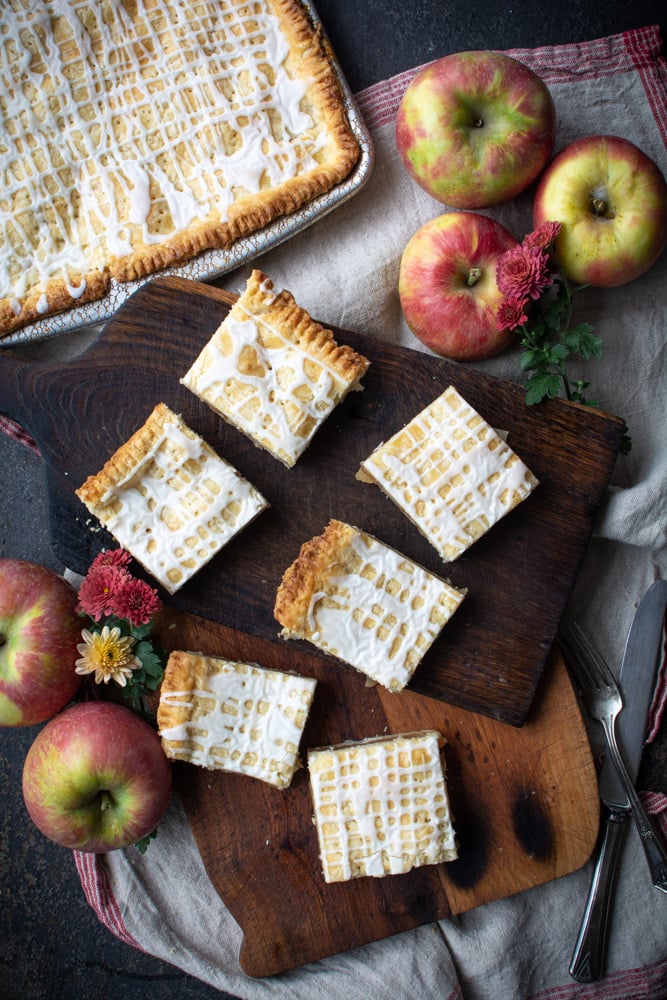 Overhead shot of slab apple pie cut into squares on a cutting board.