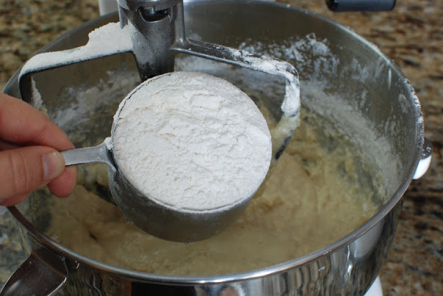 A cup of flour being added to donut dough mixture