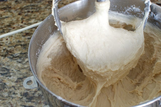 Donut dough in the bowl of an electric mixer with dough on paddle.