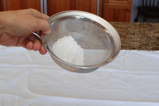 White cloth on counter with flour sifting over the top