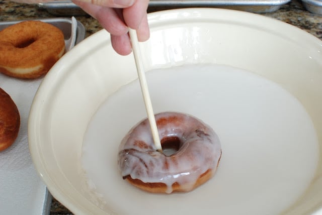 Spudnut in glaze lifting out of glaze with chopstick