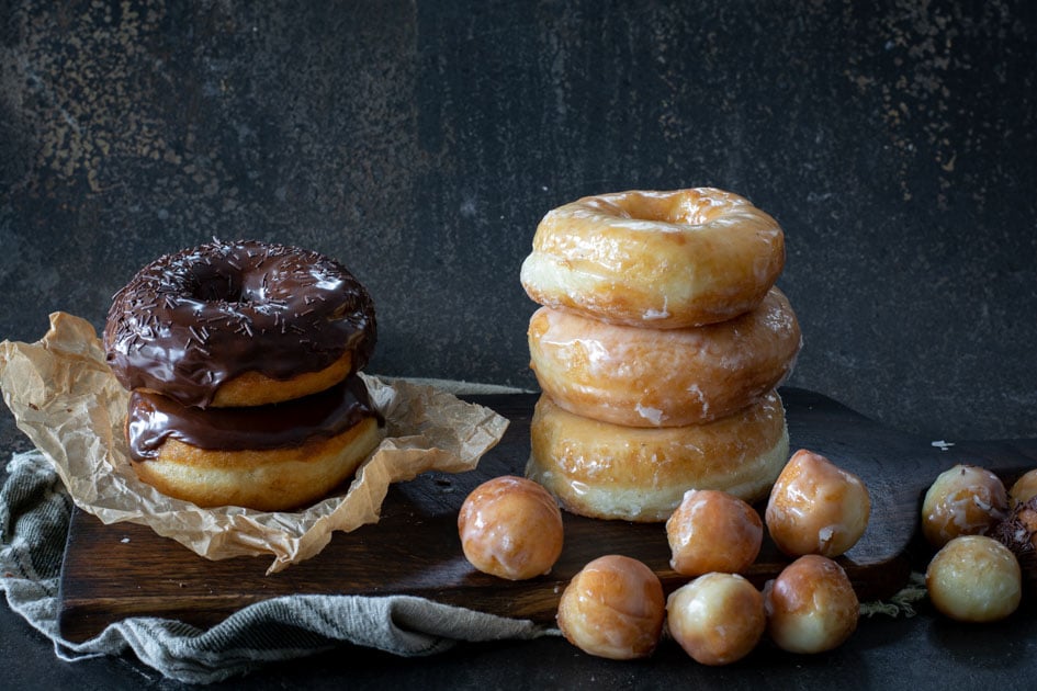 glazed spudnuts stacked on wooden board surrounded by donut holes