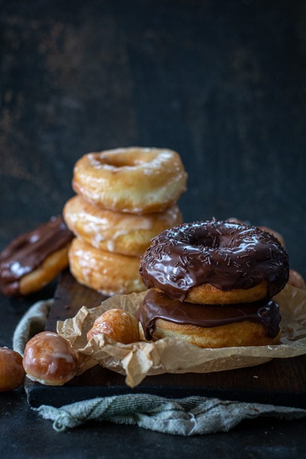 chocolate glazed and glazed spudnuts stacked on cutting board with donut holes