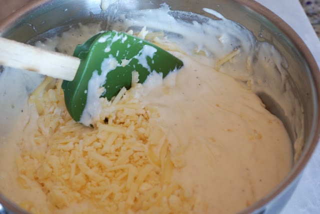 cheese being stirred into cream mixture with green spatula