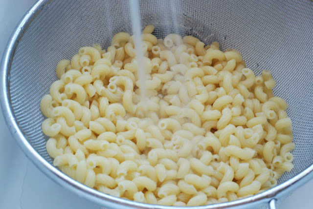 Cooked macaroni in a strainer with water running