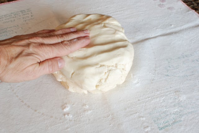 Hand pressing shortbread dough on a floured mat.