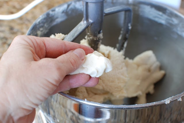 Bowl of shortbread dough with a hand holding a piece of formed dough