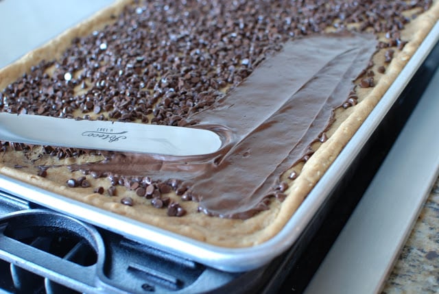 Metal spatula spreading melted chocolate over baked bars