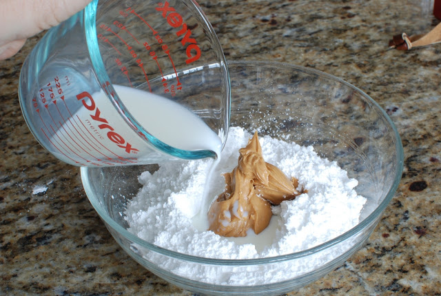 Powder sugar in a bowl with peanut butter and milk pouring over.