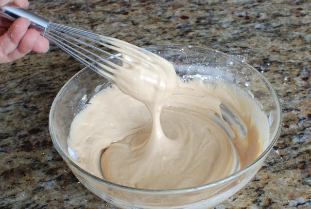 Peanut butter glaze in a bowl with wire whisk stirring glaze