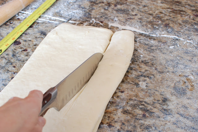 Hand with large knife cutting the dough longways/