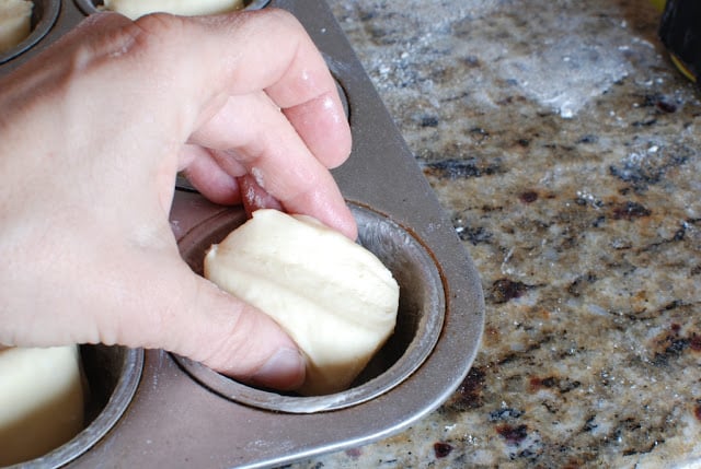 Hand putting one portion of butter flake dough into a muffin tin.