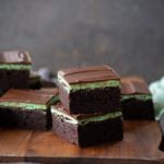 Two stacked chocolate mint brownies on a wooden cutting board