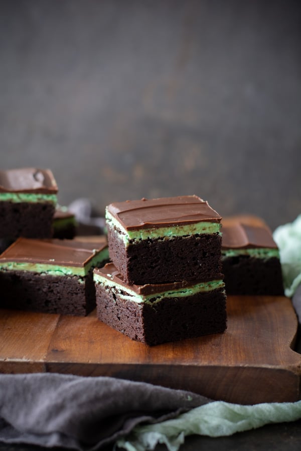 Two stacked chocolate mint brownies on a wooden cutting board