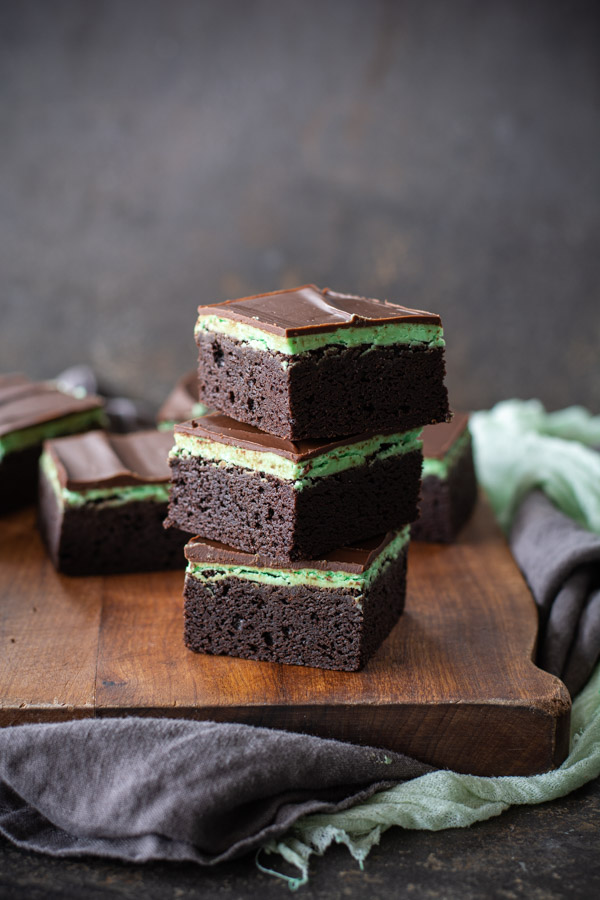Three chocolate mint brownies stacked on wooden cutting board