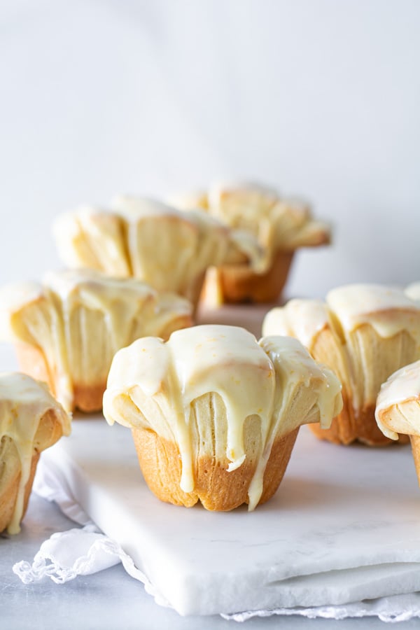 Several orange glazed butterflake rolls on a white marble tray.