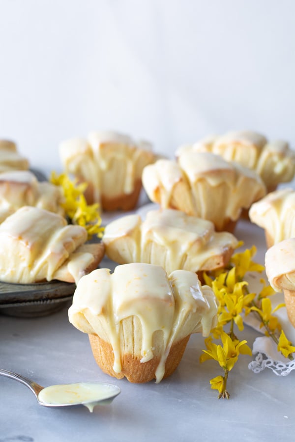 Several orange glazed butterflake rolls on a white marble tray with yellow forsythia blossoms.