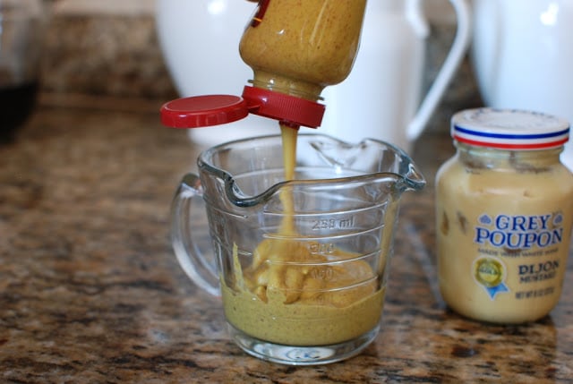 Brown mustard squeezed intro a measuring cup.