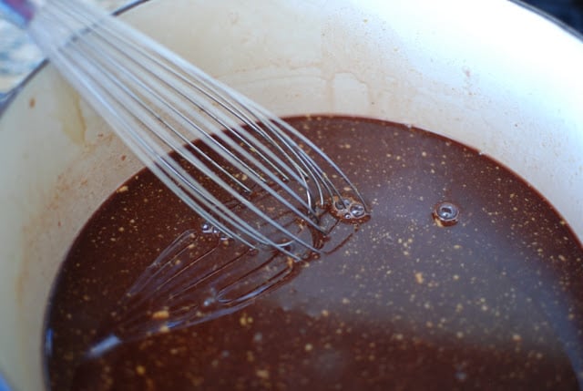 Whisking cherry cola glaze ingredients in a blue pot.