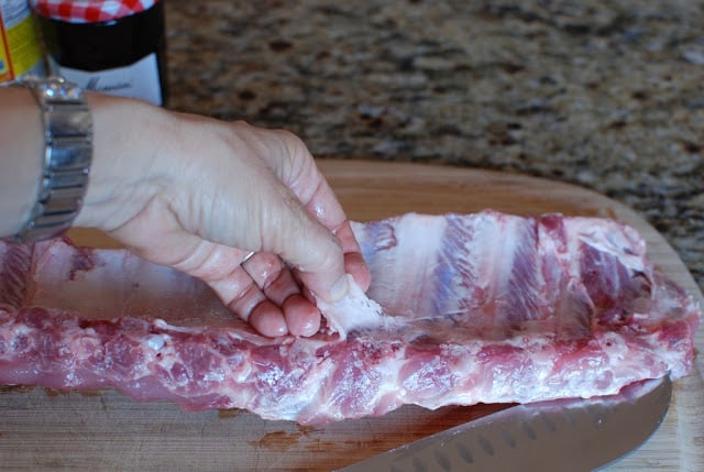 Hand pulling silverskin off of a rack of ribs.
