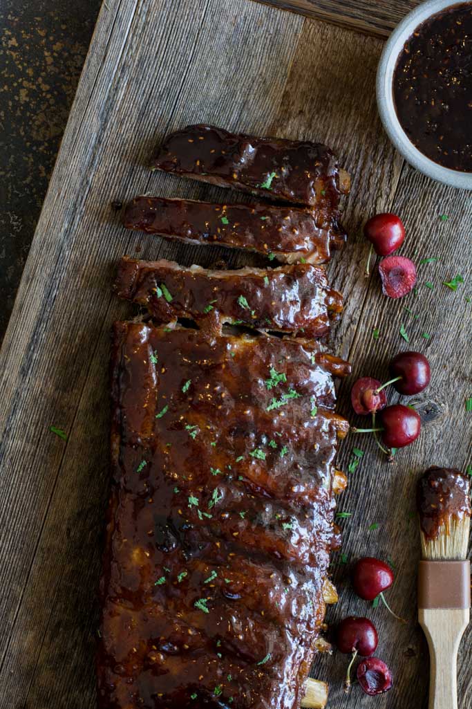 Glazed ribs on a wood board with cherries along the side