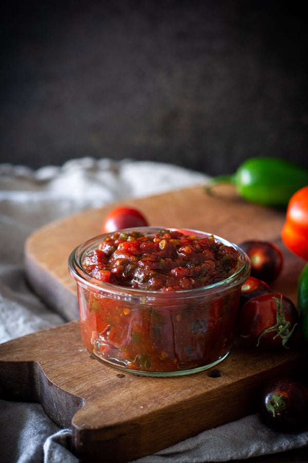 Jar of tomato jam on a cutting board with fresh tomatoes