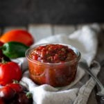 Jar of tomato jam on a linen towel with tomatoes and jalapeno peppers scattered