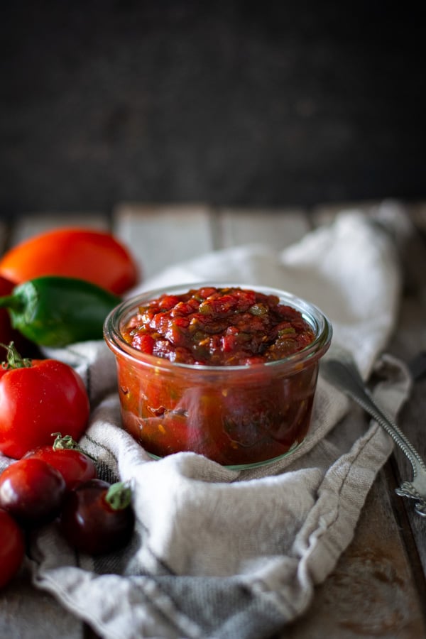 Jar of tomato jam on a linen towel with tomatoes and jalapeno peppers scattered