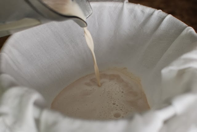 cloth lined strainer with almond milk pouring through