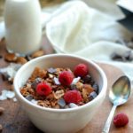 bowl of granola with fresh raspberries, spoon and milk