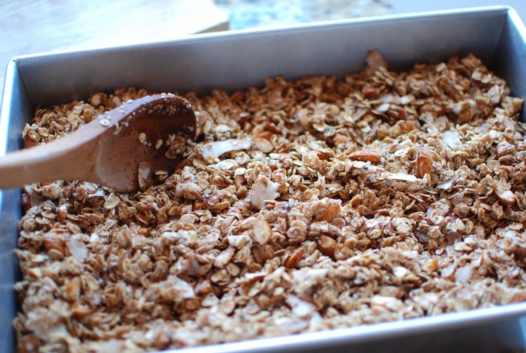 Wooden spoon stirring granola in baking pan