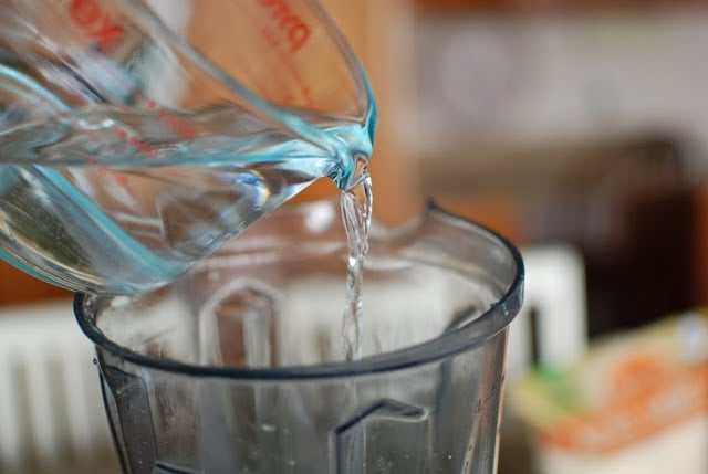 measuring cup of water pouring into blender
