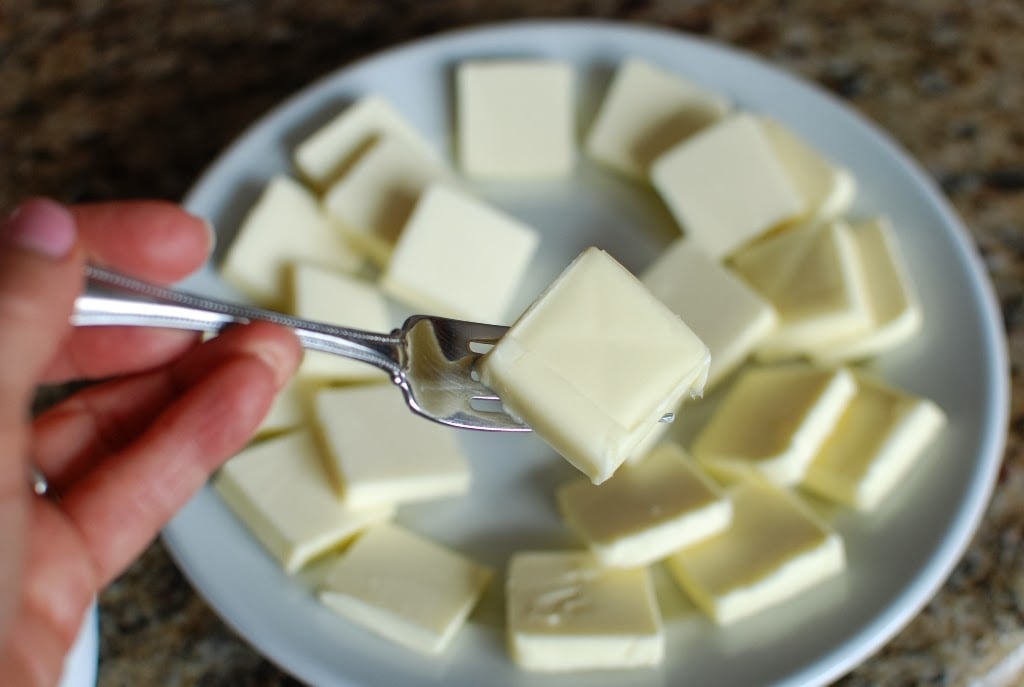 A pat of butter on a fork with plate of butter slices in background
