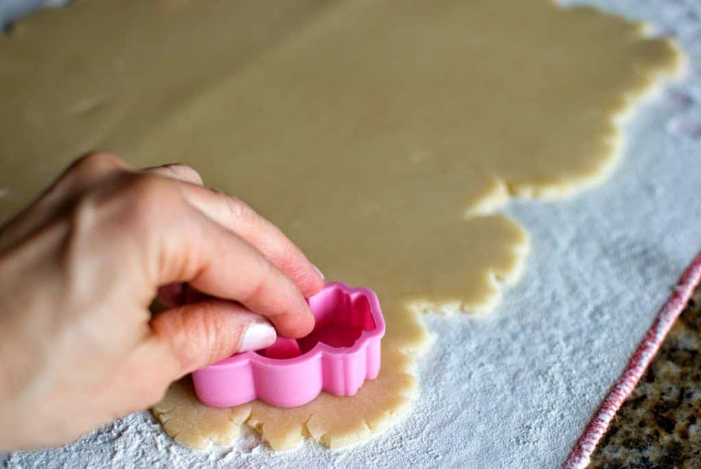 Hand pressing a pink rabbit cookie cutter into a section of flat cookie dough.