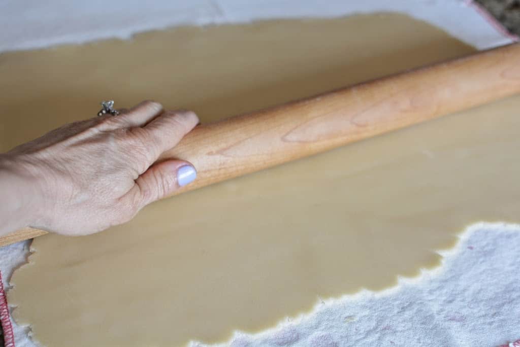Hand with wooden rolling pin, rolling out cookie dough on a white surface.