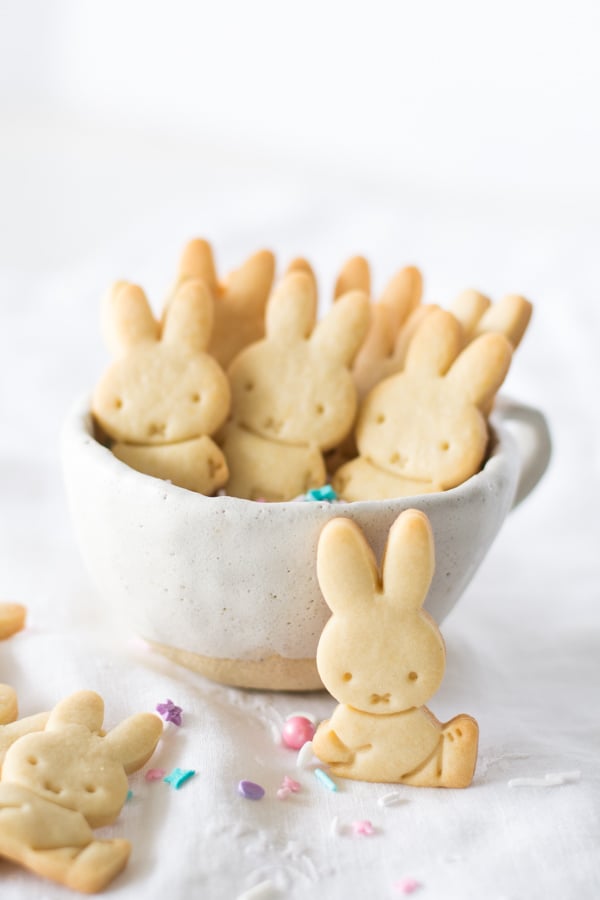 Several Miffy Petit Beurre bunny cookies in a white bowl with colorful pastel sprinkles. A few more bunnies are scattered around the bowl with additional sprinkles.