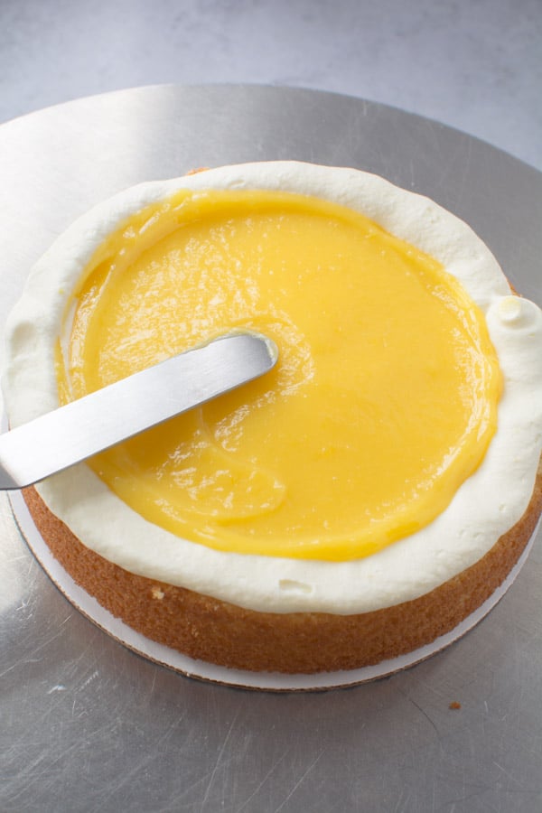 lemon curd being spread on a cake layer
