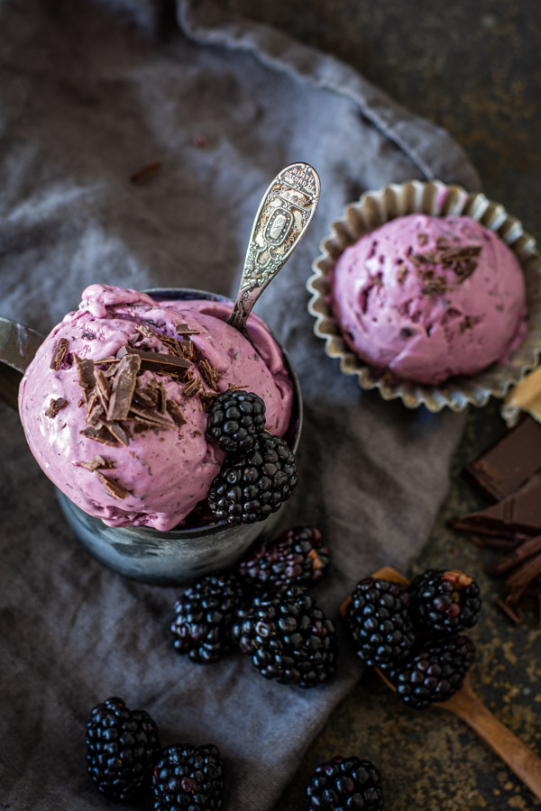 overhead shot of blackberry chocolate chip ice cream in tin mug with spoon, blackberries, and chopped chocolate