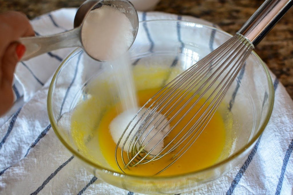 Adding sugar to the glass bowl with whisked eggs.