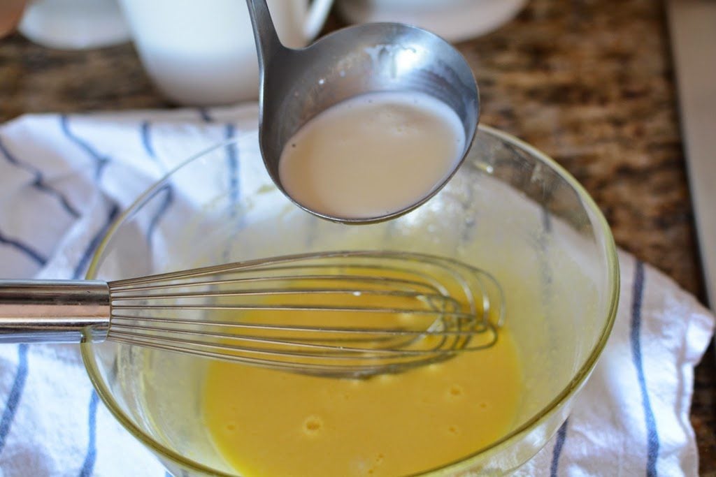 Adding cream mixture to eggs and sugar in a glass bowl.