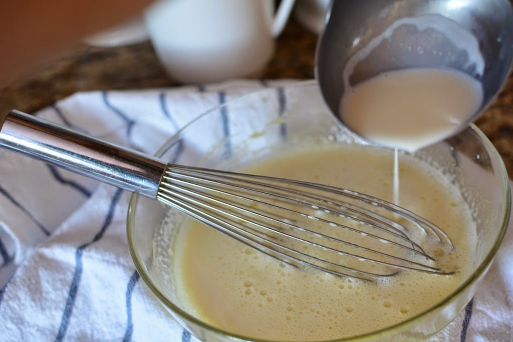 Adding hot liquid to eggs and sugar in glass bowl.