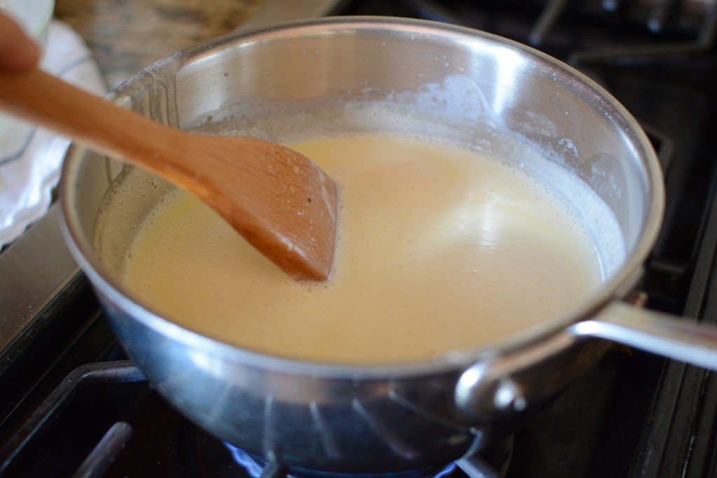 Lemon curd ice cream mixture cooking in a saucepan on the stove.