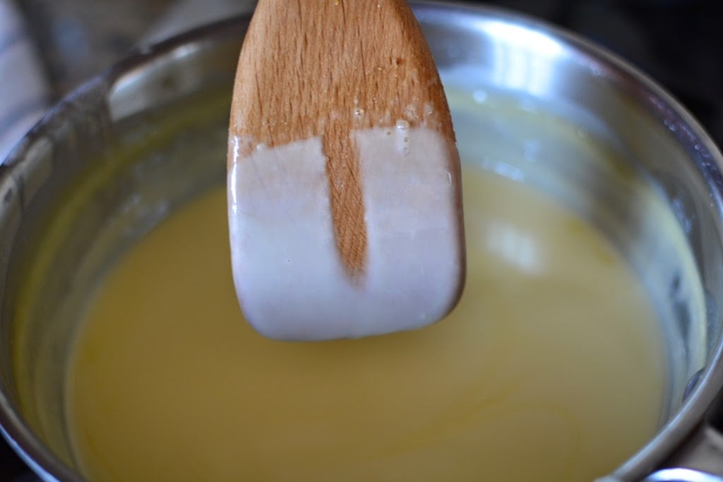 Wooden spoon dipped in cooking custard with finger trail across the custard