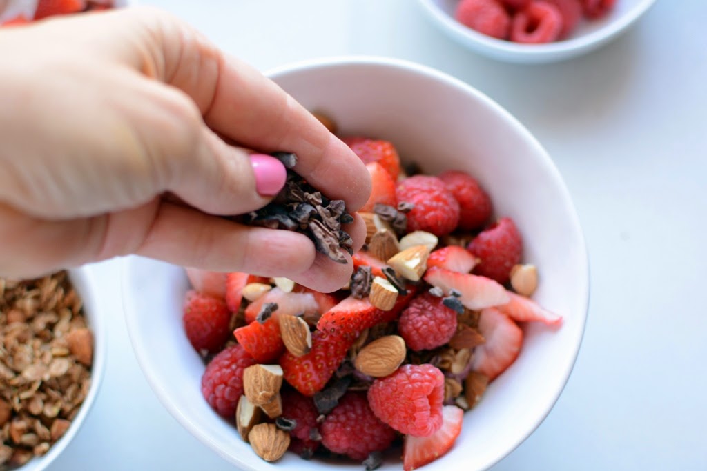 White bowl with berries, almonds with hand sprinkling cacao nibs