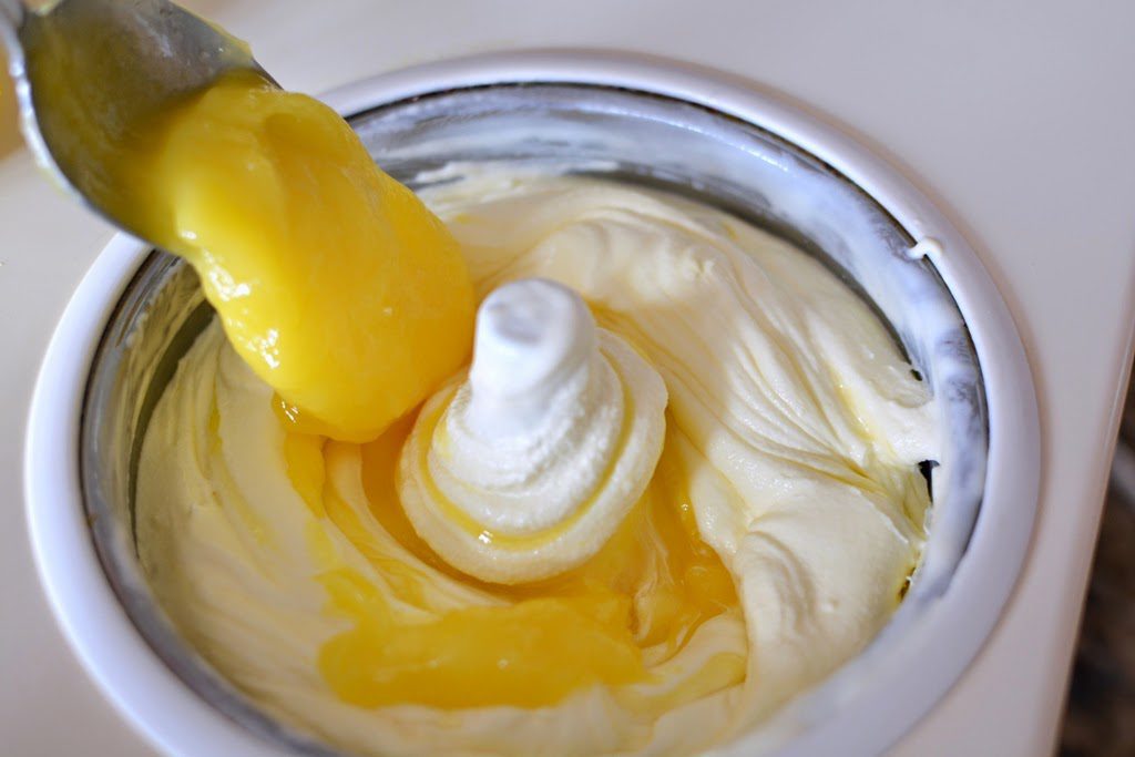 Adding bright yellow lemon curd to vanilla ice cream in a mixer.