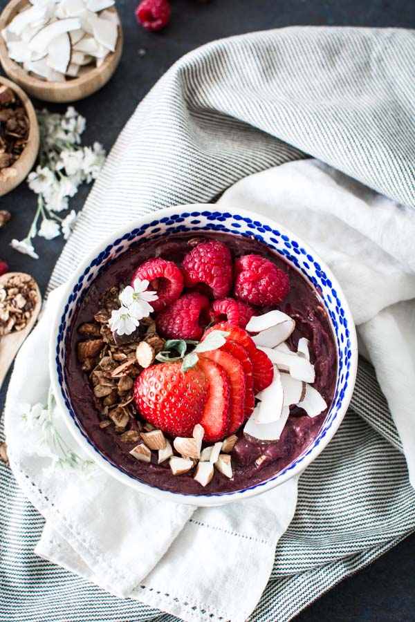 Close up picture of Acai bowl topped with berries, coconut, almonds on striped cloth
