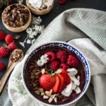 Acai bowl with fresh berries on a striped cloth with granola and coconut in small wooden bowls