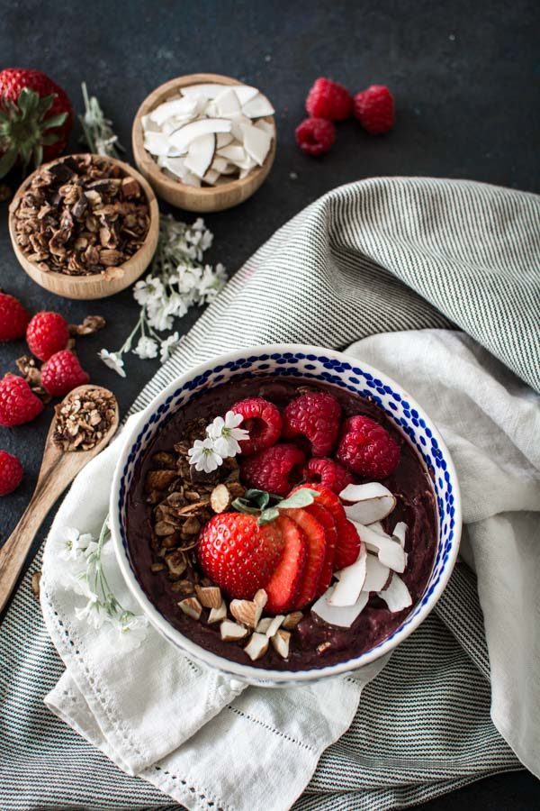 Acai bowl with fresh berries on a striped cloth with granola and coconut in small wooden bowls
