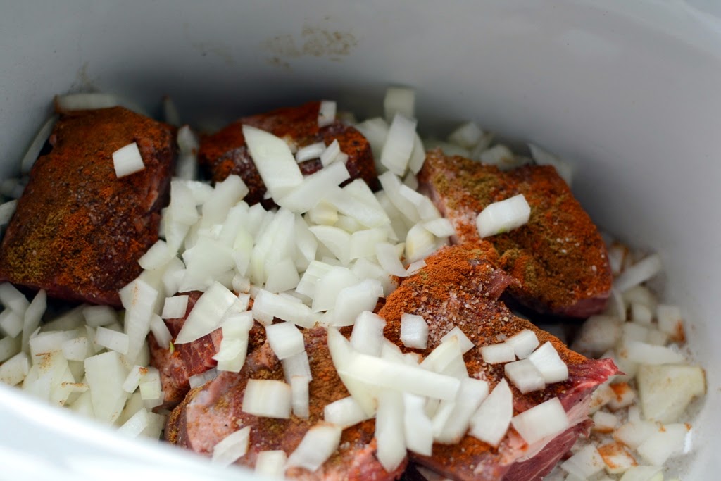Uncooked beef in crockpot with spices and onions