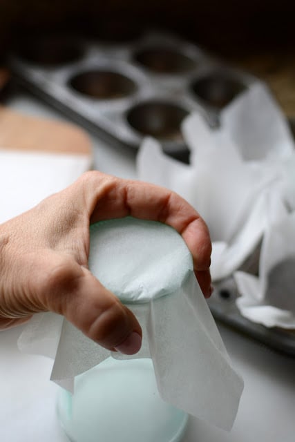 Hand placing a piece of parchment paper over a glass to create a muffin wrapper.